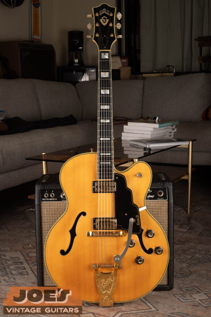 Full-body shot of a high-end 1960s Guild X-500 archtop electric guitar in sunburst finish, featuring a factory-installed Bigsby vibrato tailpiece, gold hardware, and multi-ply binding.