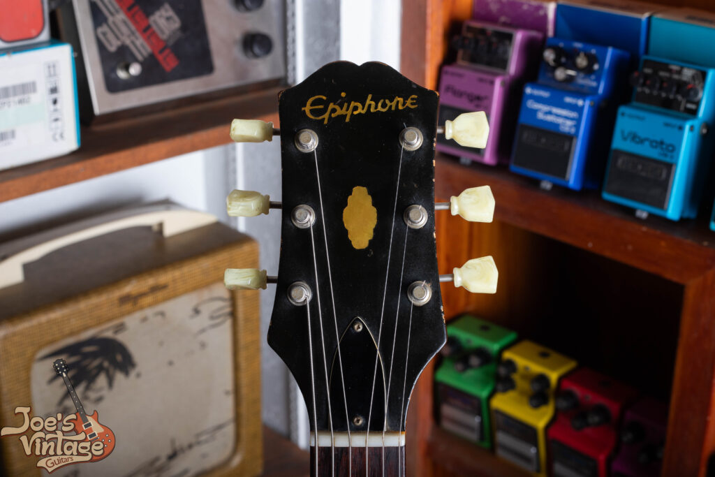 Close-up of a 1961 Epiphone Crestwood headstock featuring the early symmetrical three-per-side tuner configuration and the raised metal Epiphone logo plate.