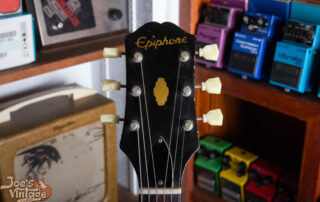 Close-up of a 1961 Epiphone Crestwood headstock featuring the early symmetrical three-per-side tuner configuration and the raised metal Epiphone logo plate.