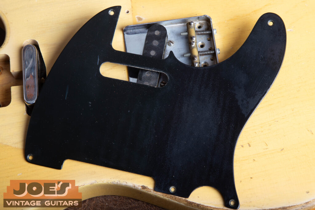 Close-up of an original 1952 Fender Telecaster black phenolic pickguard showing authentic lacquer wear and play marks on the surface.
