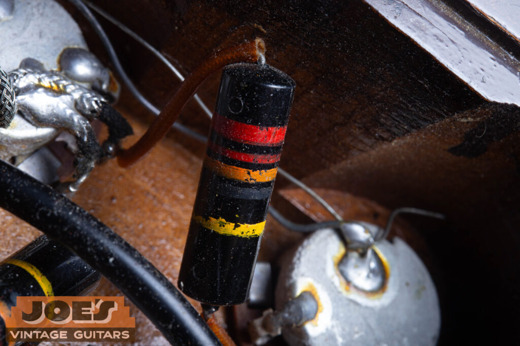 Macro close-up of an original 1956 Sprague "Bumblebee" capacitor (.022uF 400V) inside the control cavity, showing the distinct color-coded stripes.