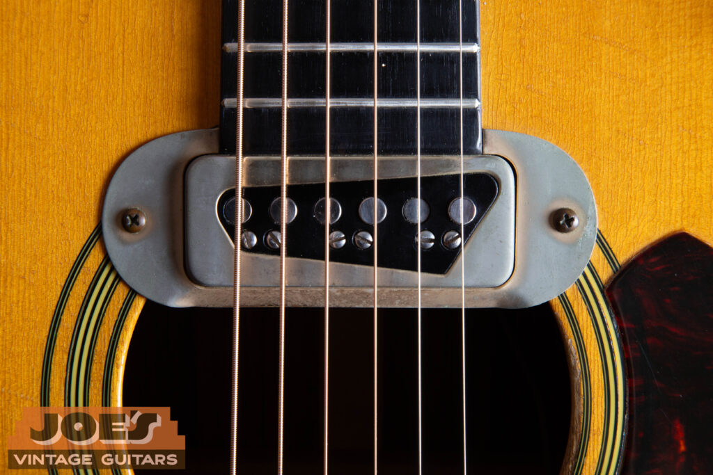 Close-up of a vintage DeArmond single-coil pickup factory-installed on a Martin D-28E, showing the chrome casing and adjustable pole pieces.