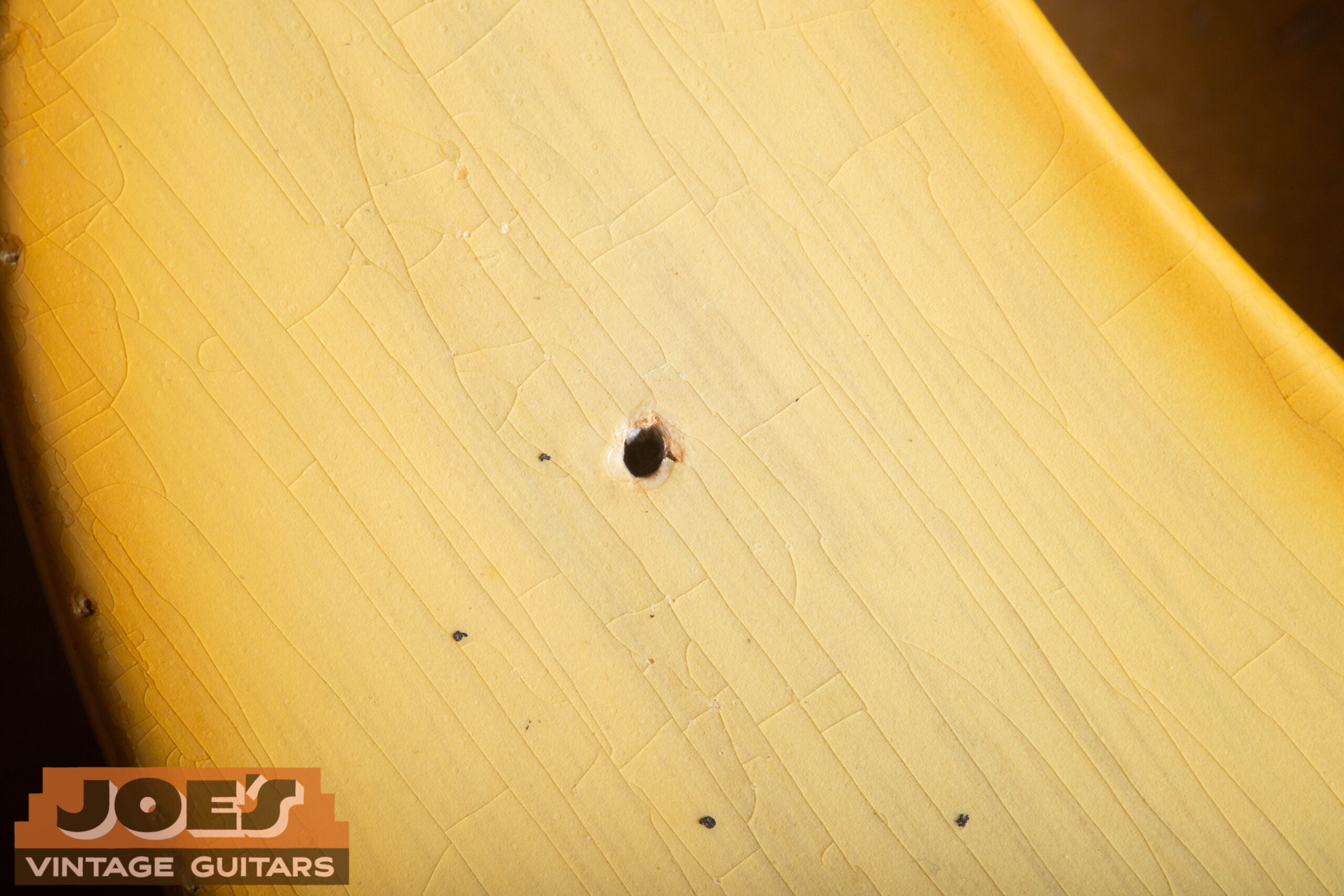 Nail holes in a 1952 Fender Precision Bass finish showing bare wood at center — the nail was removed after spraying, leaving a clean hole through the lacquer to bare wood