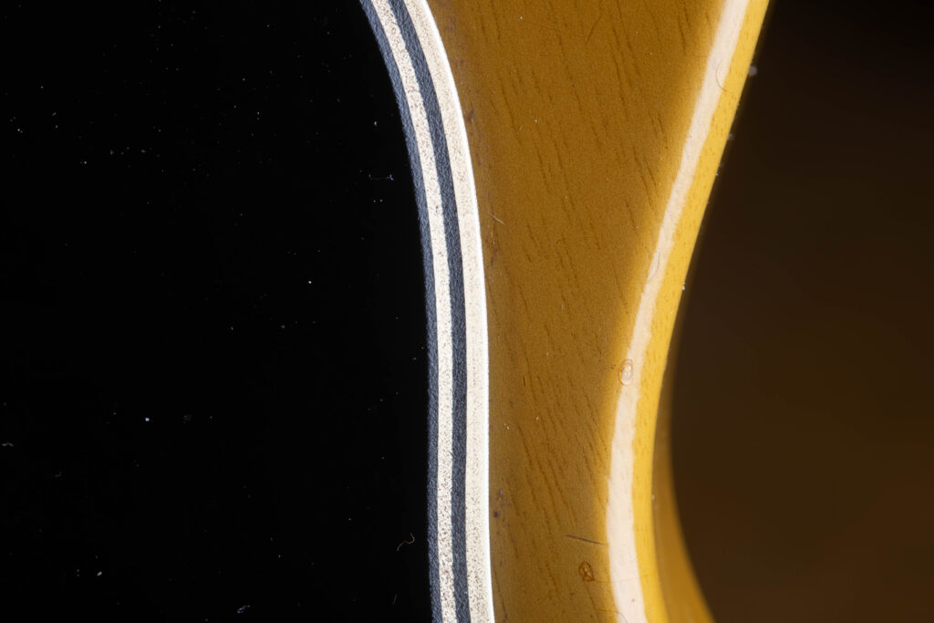 Side-angle perspective of an original 1957 Gibson Les Paul Special pickguard, showcasing the distinct 5-ply laminate construction. The edge clearly displays the alternating layers of Black/White/Black/White/Black plastic, with visible signs of natural aging, slight beveling from the factory, and minor surface scratches characteristic of "Golden Era" use.