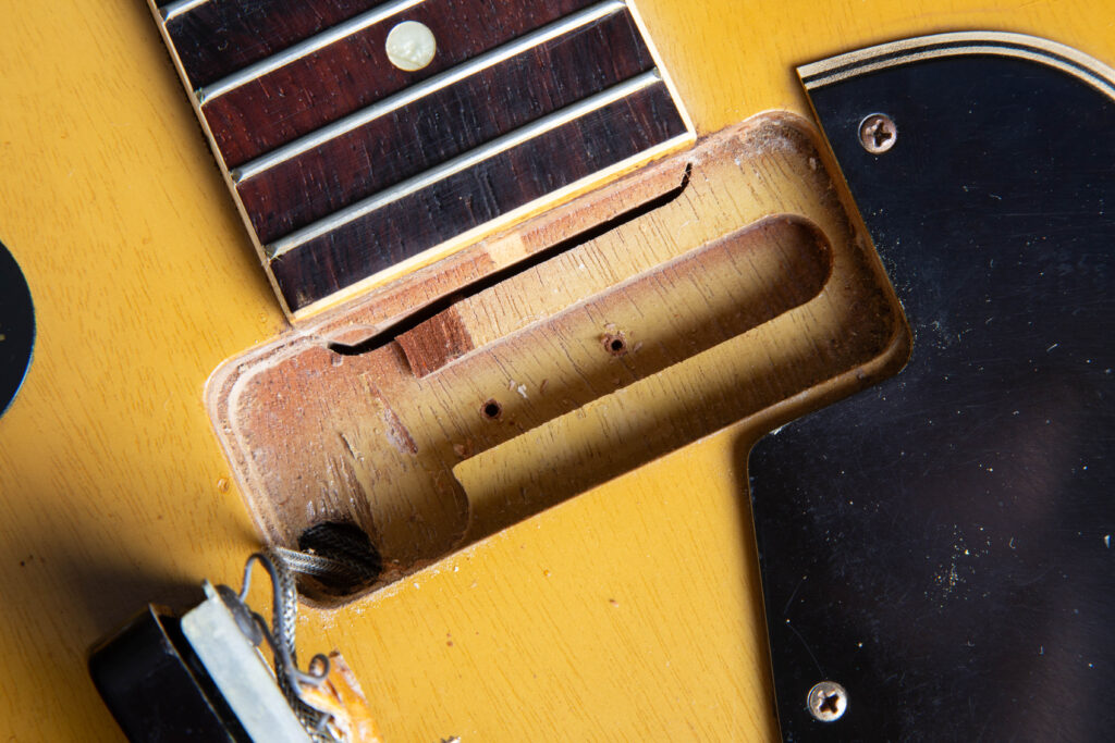 Top-down macro view of a 1957 Gibson Les Paul Special neck pickup routing. The image highlights the distinctive slim channel at the base of the cavity and the exposed end of the mahogany neck tenon. Detailed features include the original "Golden Era" mahogany wood grain, factory-drilled mounting holes, and the translucent TV Yellow nitrocellulose finish bleeding over the routed edges.
