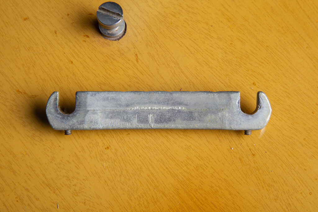 Close-up rear view of an authentic 1957 Gibson Les Paul Special nickel-plated wraparound tailpiece. Detail highlighting the original "short seam" casting line and the two factory-original intonation Allen screws located near the bridge posts. The nickel plating shows natural 1950s patina and oxidation.