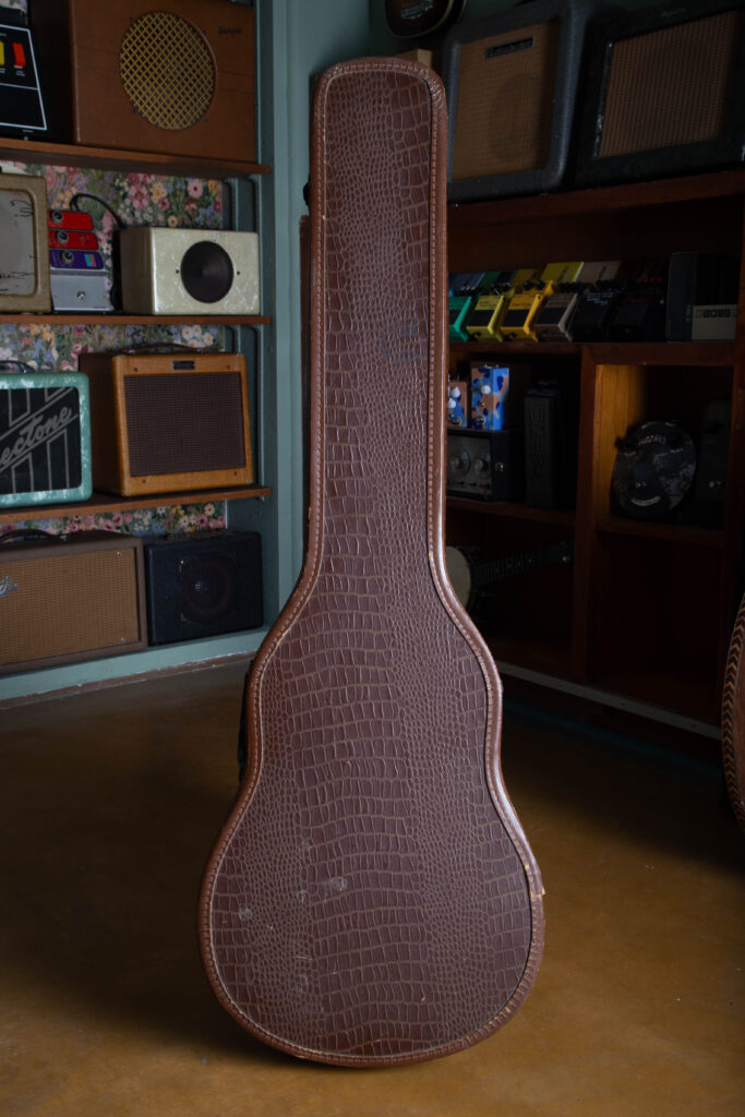 Alt Text A wide perspective of an original 1950s Gibson "alligator" chipboard guitar case. The image highlights the distinctive textured exterior that mimics the look of alligator skin, along with the vintage-style plastic handle, metal latches, and the characteristic slim, tapered silhouette designed specifically for the 1955–1958 Les Paul Special body style.