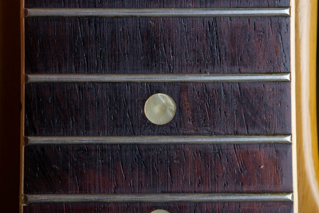 A detailed perspective of an original 1958 Gibson Les Paul Special fretboard dot inlay. The image captures the organic, "wavy" texture of the mother-of-pearl material, showcasing a distinct iridescent shimmer and subtle greenish-grey tinting caused by decades of natural aging on the dark rosewood fingerboard.