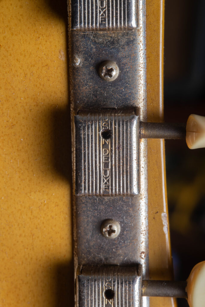 Macro view of the back of 1958 Gibson Les Paul Special headstock featuring original nickel-plated Kluson Deluxe "3-on-a-strip" tuners. The image highlights the "Kluson Deluxe" stamped vertically on each tuner casing and the original plastic buttons. The mahogany wood displays a black ink-stamped serial number and fine nitrocellulose lacquer checking characteristic of "Golden Era" craftsmanship.