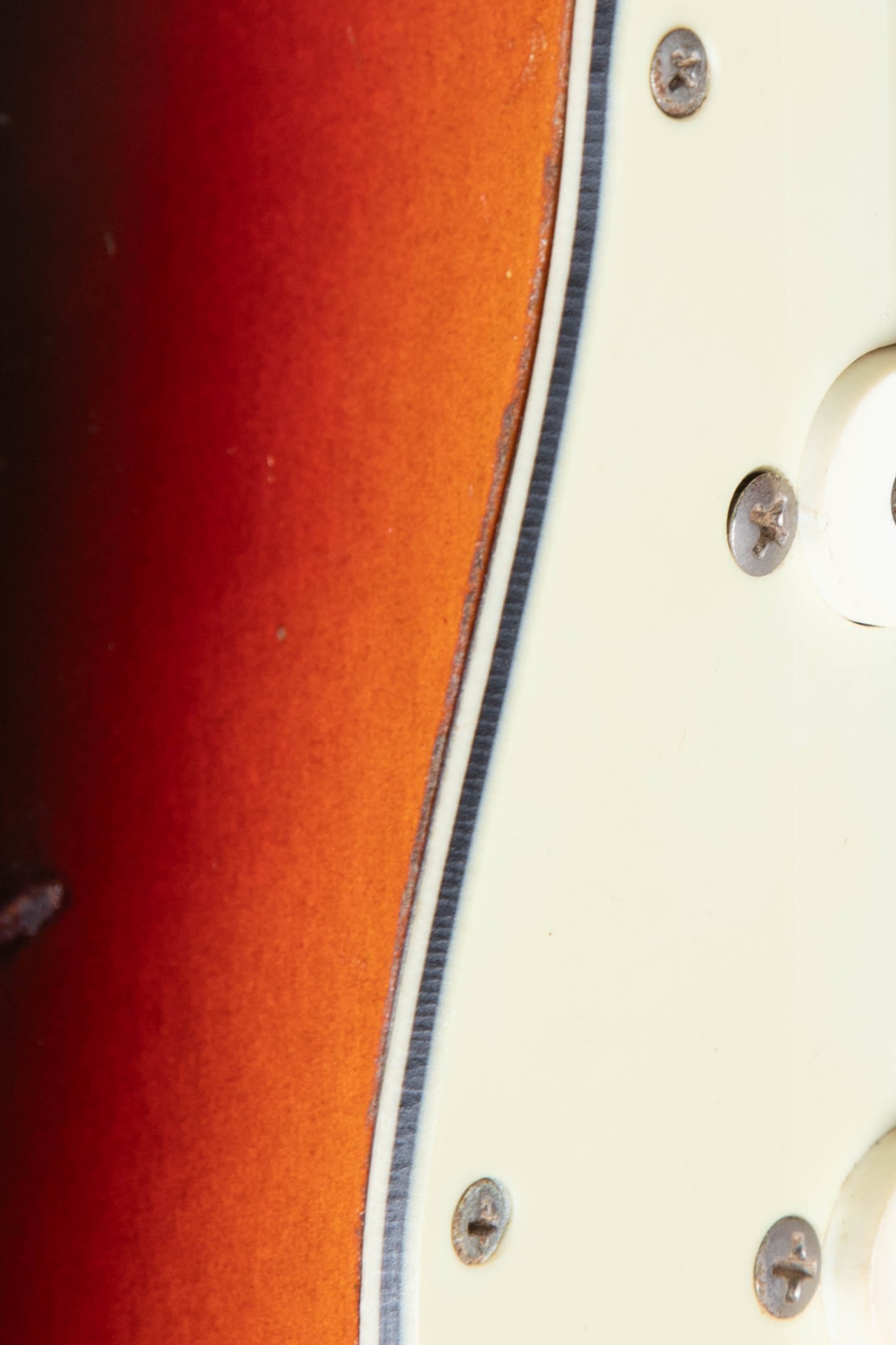 1962 Fender Stratocaster 3-ply pickguard edge close-up showing white-black-white layers with characteristic mint green aging of outer layer and slight warping