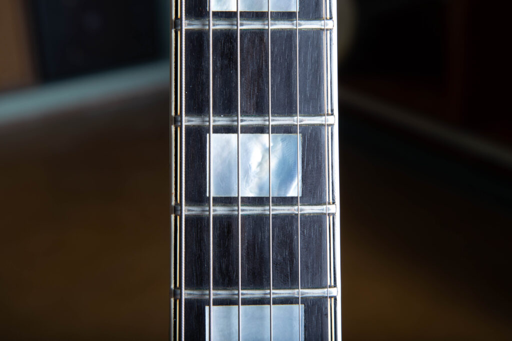 Close-up of a Gibson L-5 CES fingerboard featuring a large rectangular block inlay made of shimmering mother-of-pearl. The inlay is set into a dark, premium ebony fretboard, bordered by multi-ply white and black binding and polished nickel frets.