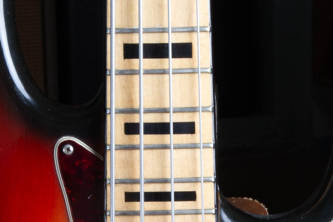 Close-up of the 1973 Fender Jazz Bass maple fingerboard showing white binding, bold black block inlays, and the warm amber tone the maple has developed under the lacquer