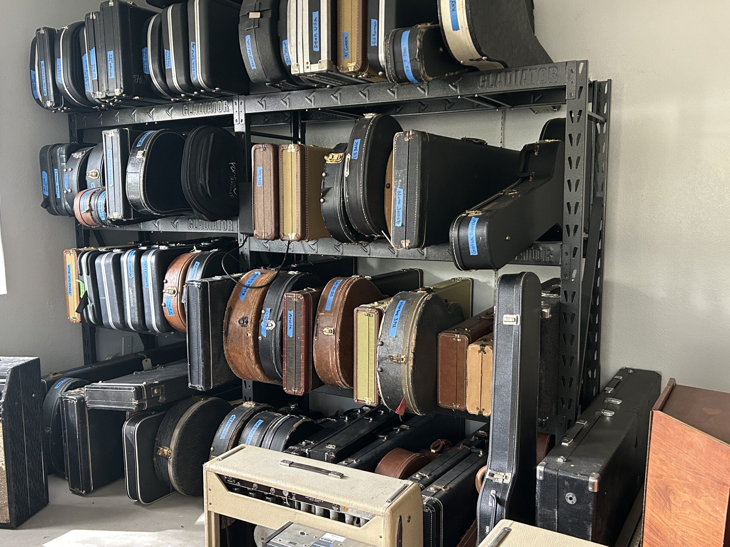 A large guitar collection stored in cases on a rack — the kind of inherited collection Joe's Vintage Guitars evaluates and purchases